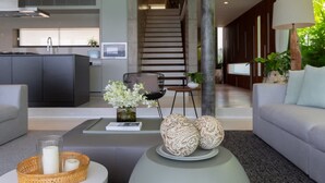 Una sala de estar moderna con un sofá, una mesa de centro y elementos decorativos. Una escalera conduce a un nivel superior.