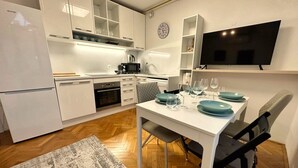 A modern kitchen with white cabinets, a built-in oven, a microwave, and a dining area with a table set for four. - Charming City Loft Apartment With Free Parking (Ljubljana)
