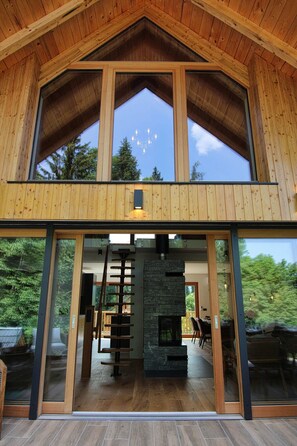 Une structure moderne en bois, dotée d’une grande entrée vitrée, d’une cheminée en pierre et offrant une vue sur l’extérieur.