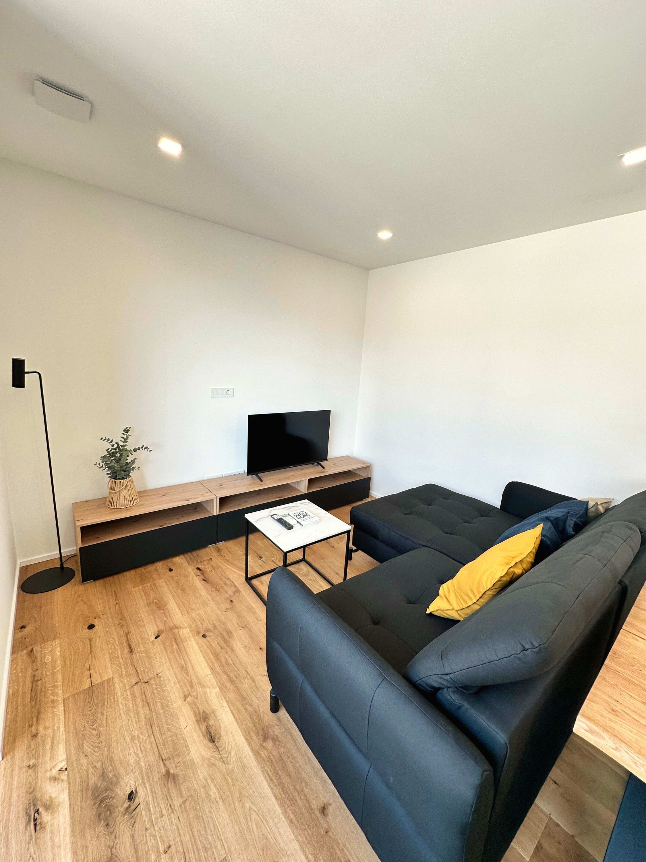 A modern living room with a black sofa, a small coffee table, a TV on a wooden stand, and a floor lamp.