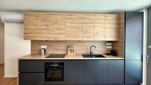 A modern kitchen with wooden cabinets, a black countertop, a built-in oven, and a refrigerator. - Garden Residence - Premium Downtown Apartment (Ljubljana)