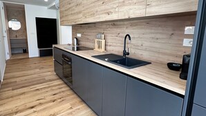 A modern kitchen with wooden cabinetry, a black sink, and a stainless steel kettle. - Garden Residence - Premium Downtown Apartment (Ljubljana)