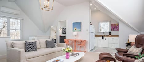 A spacious loft with a high ceiling, a dining area with a table and chairs, a kitchen with white cabinets, and a living room with a sofa and coffee table.