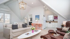 A spacious loft with a high ceiling, a dining area with a table and chairs, a kitchen with white cabinets, and a living room with a sofa and coffee table.