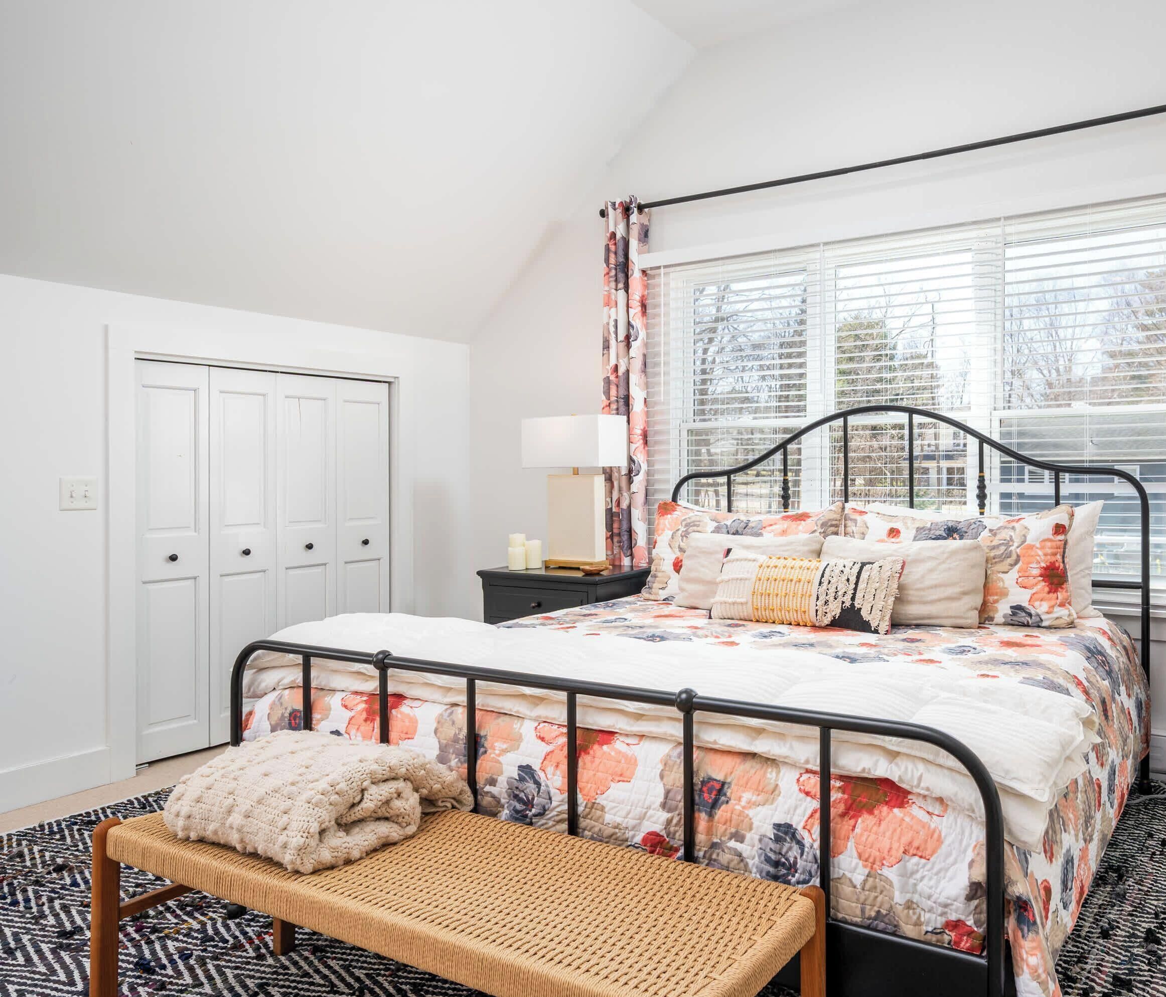 A bedroom with a bed, bedside table, lamp, and a bench.