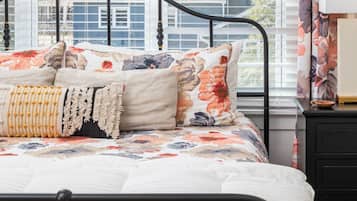 Una cama con una colcha estampada con motivos florales, una almohada decorativa color beige y un cobija de cuentas amarillas.