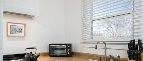 Una cocina con estufa, horno tostador, fregadero y ventana con persianas.
