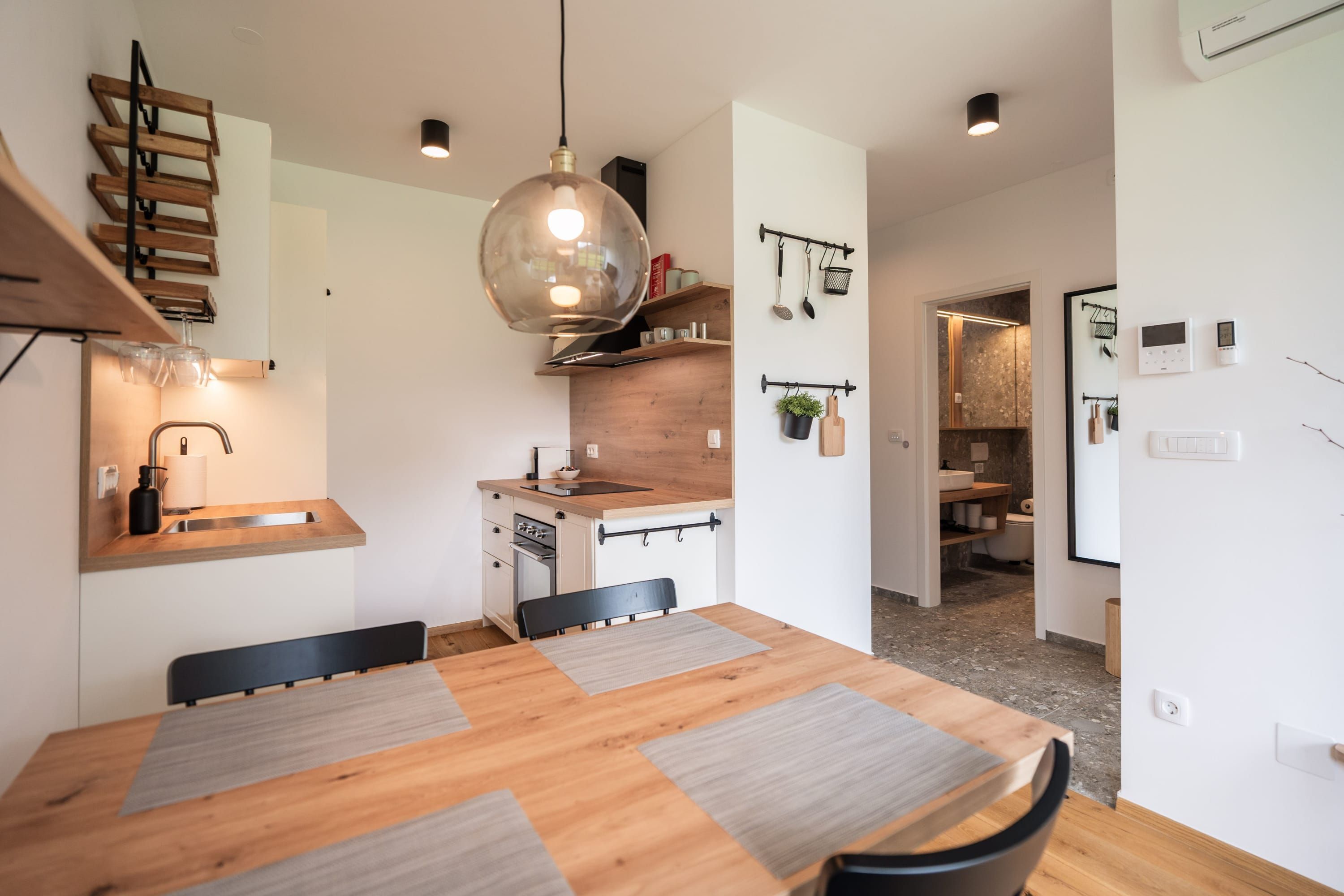 Une cuisine moderne avec une table à manger en bois, un luminaire suspendu et un four encastré.