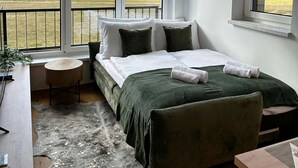 A bedroom with a large bed, a desk, and a view of a mountainous landscape through large windows. - So a Valley Suites - Superior Apartment 09 (Bovec)