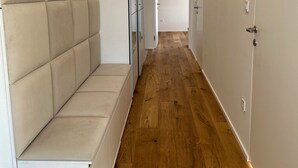 Ein schmaler Flur mit Holzdielen, weißen Wänden und einer beige bezogenen Bank.