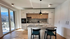 Una cocina moderna con una isla grande, dos taburetes de bar y vistas al exterior por una puerta corrediza de vidrio.