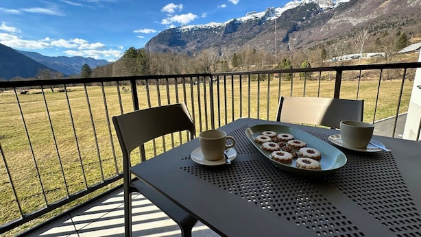 Un balcón con una mesa lista para el desayuno, con vistas a un paisaje montañoso.