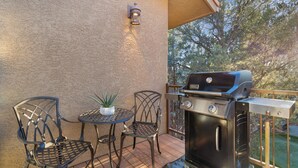 Un patio con una parrilla, dos sillas y una mesa pequeña con una planta.