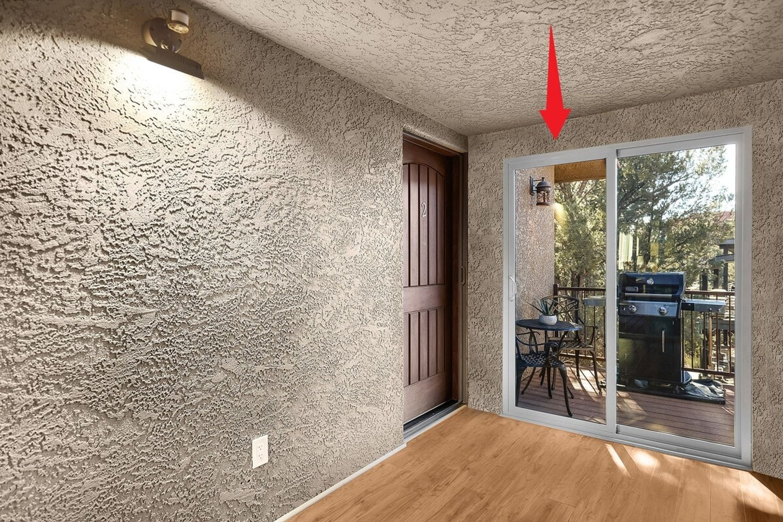 A room with textured walls, a wooden floor, a sliding glass door leading to an outdoor patio with a grill.