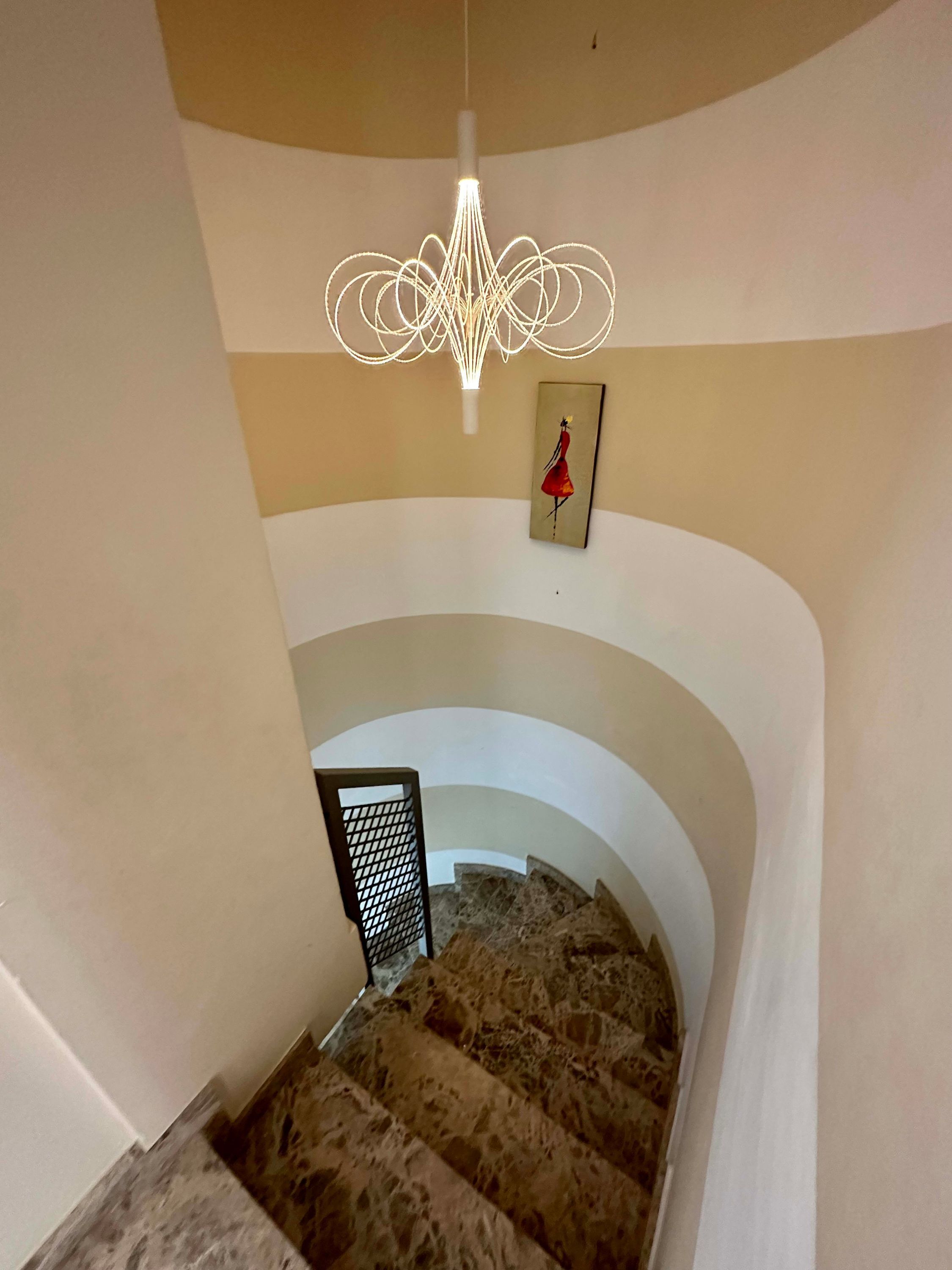A staircase with a unique light fixture and a painting on the wall.