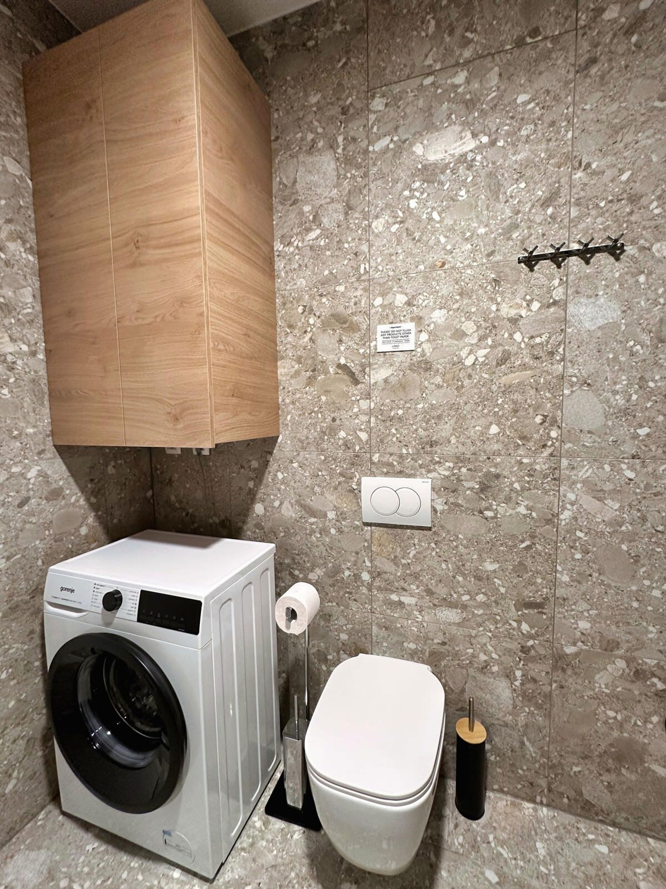 Une petite salle de bain équipée d’un lave-linge, de toilettes et d’un meuble en bois.