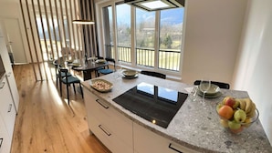 Une cuisine moderne dotée d’un grand îlot central, de planchers en bois et offrant une vue sur l’extérieur grâce à de grandes fenêtres.