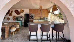 An open-plan kitchen and dining area with a stone wall, wooden furniture, and hanging lights. - Casa Con Vista - Stunning Villa in Moraira (Teulada)