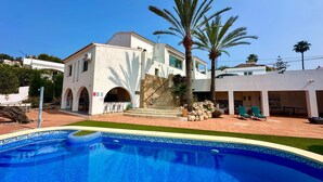 A pool with a dolphin design, a white building with arches, and palm trees. - Casa Con Vista - Stunning Villa in Moraira (Teulada)