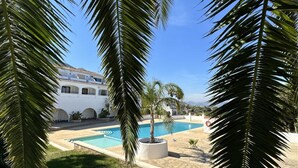 Une piscine entourée de palmiers, un bâtiment blanc orné d’arches et un ciel d’un bleu limpide.