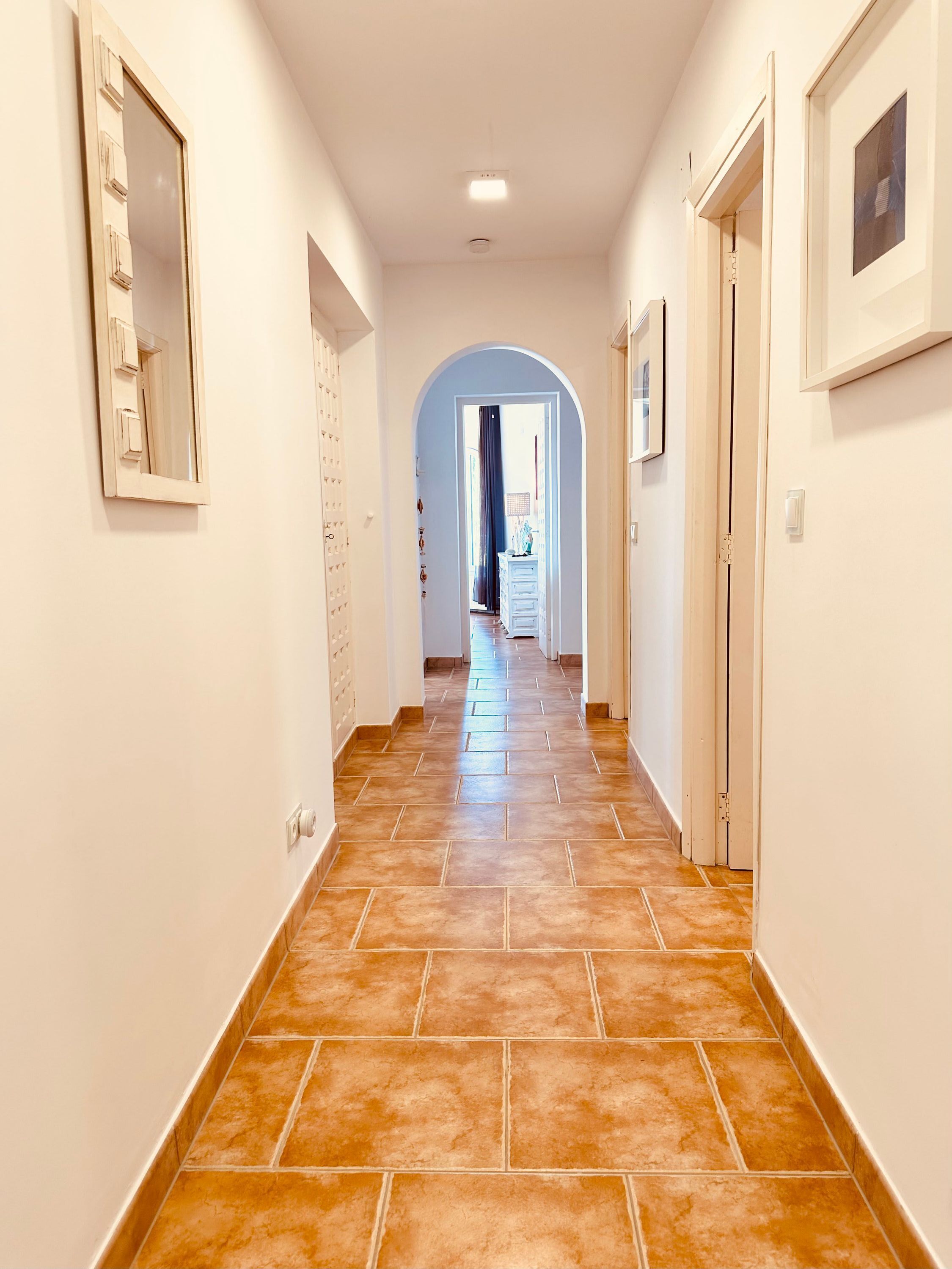 A hallway with a tiled floor, white walls, and doors on both sides.