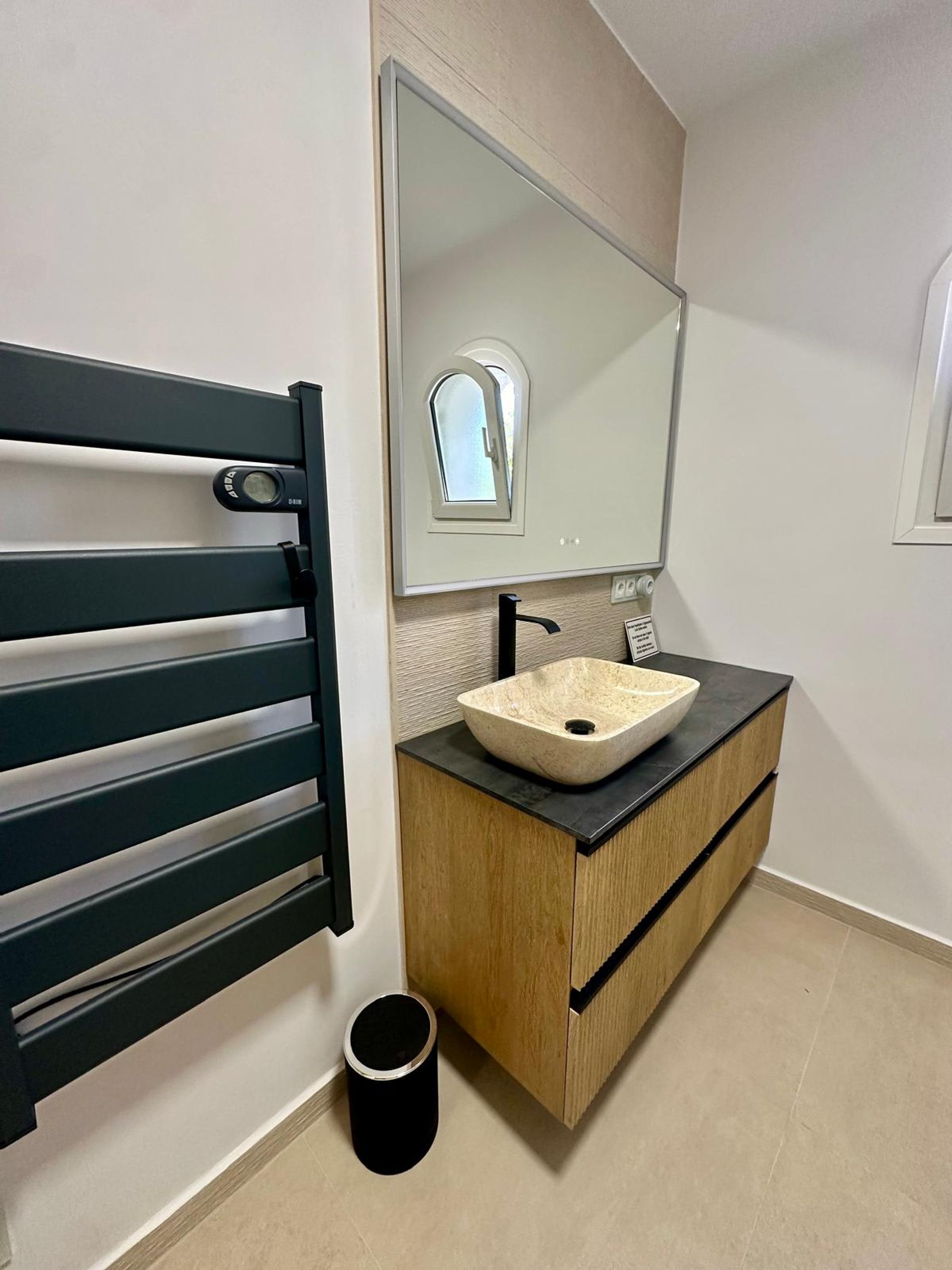A bathroom with a black towel rack, a wooden vanity with a beige sink, and a mirror above the vanity.