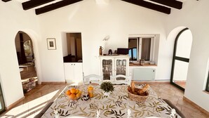 Comedor con mesa preparada para cuatro, cocina al fondo y vista a través de un arco.