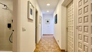 Un pasillo con piso de baldosas, paredes blancas y puertas con diseño de cuadrícula.