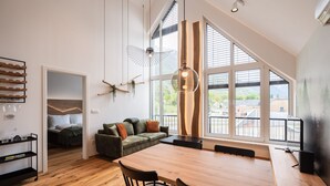 A modern living space with a wooden dining table, a green sofa, and a large window offering a view of the outdoors. - So a Valley Suites - Superior Apartment 28 (Bovec)