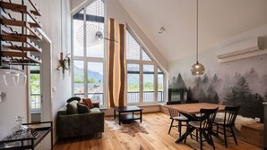 A spacious room with a large dining table, a sofa, and a view of mountains through large windows. - So a Valley Suites - Superior Apartment 28 (Bovec)