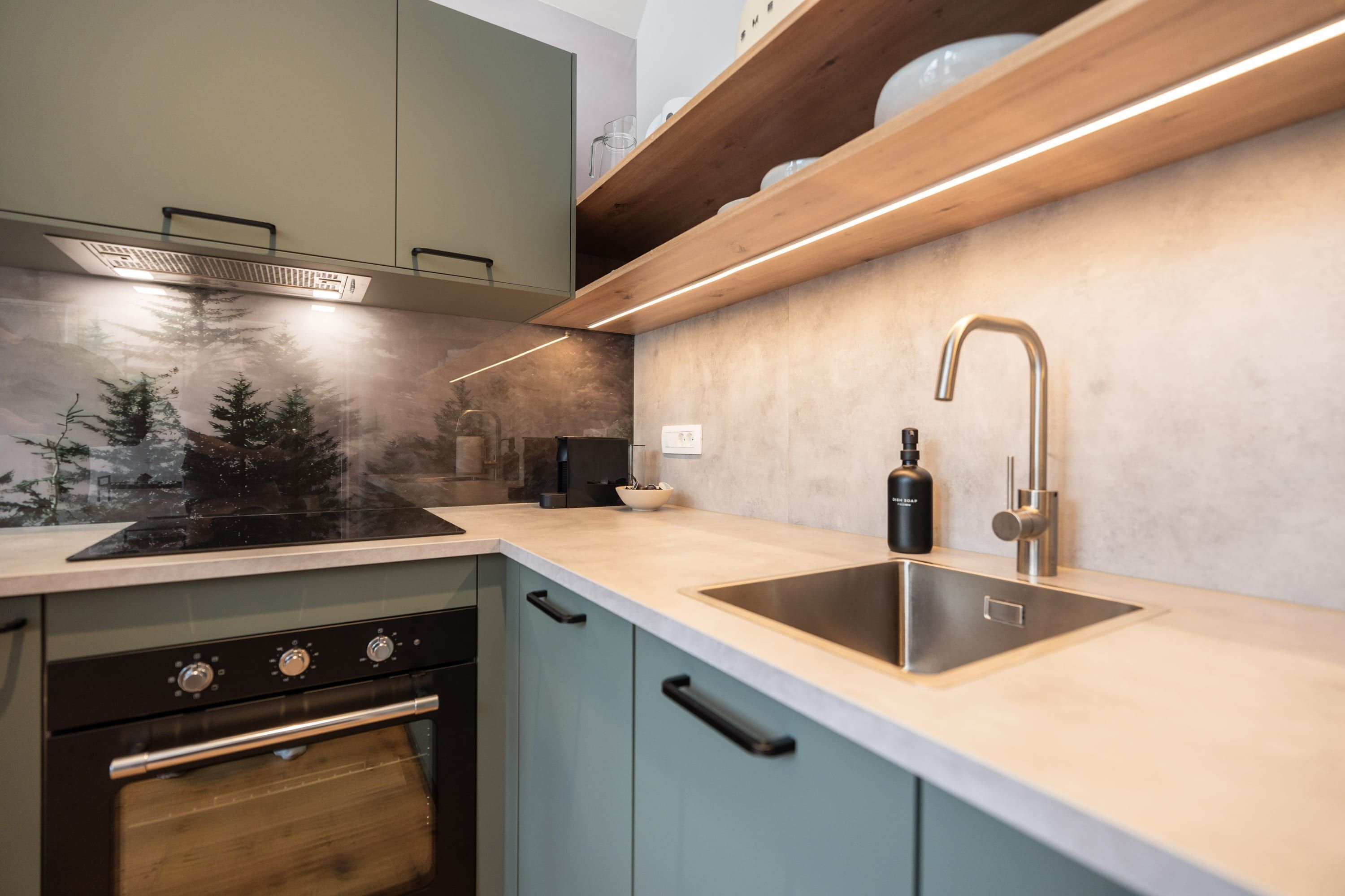 Une cuisine moderne dotée d’un four encastré, d’un évier en acier inoxydable et d’une étagère en bois au-dessus du plan de travail.