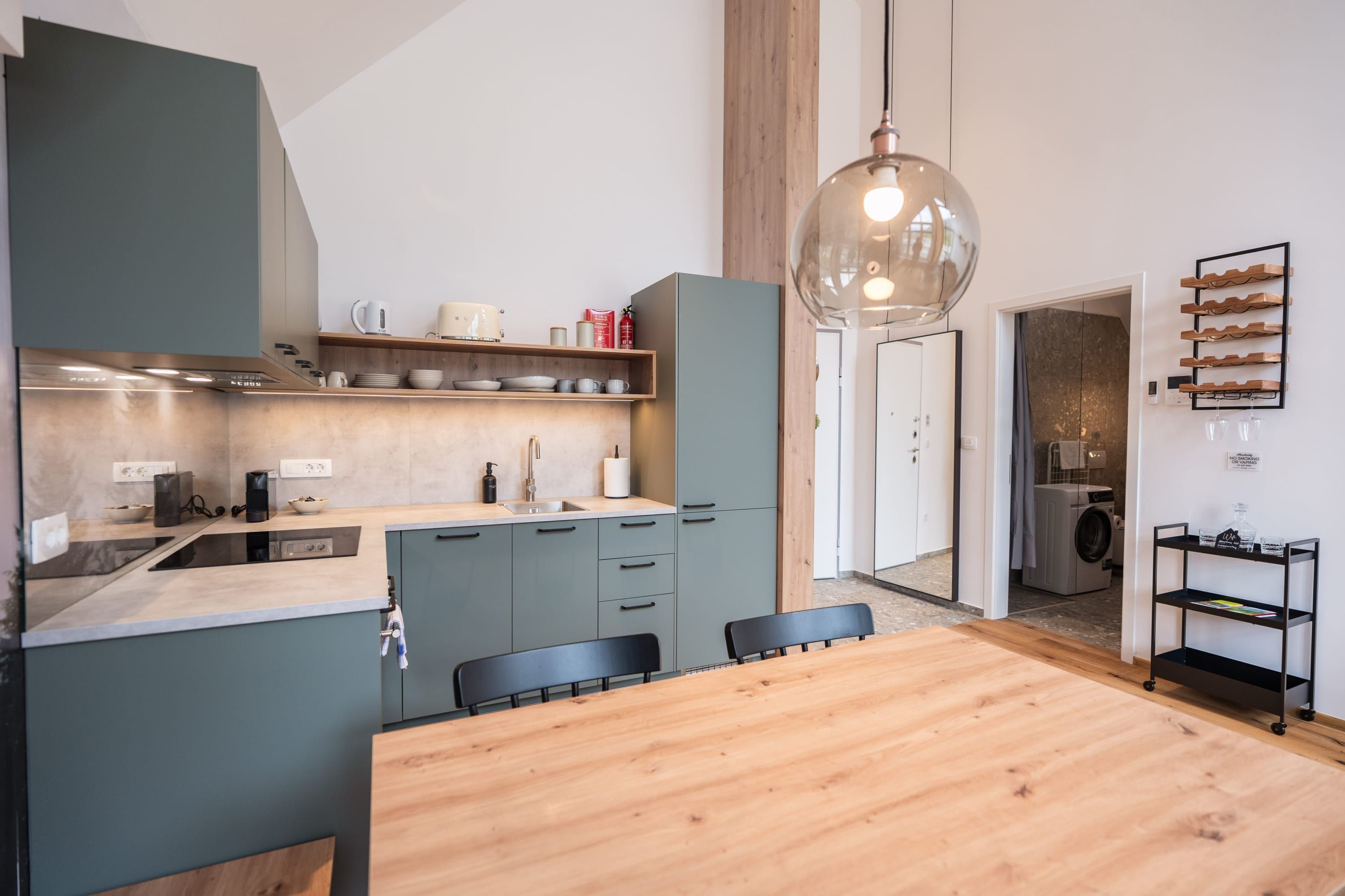 Een moderne keuken met een houten eettafel, grijze kastjes en een hangende lamp.