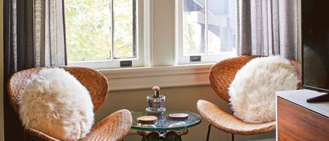 A room with two wicker chairs, a small round table with a candle, and a television on a wooden cabinet.
