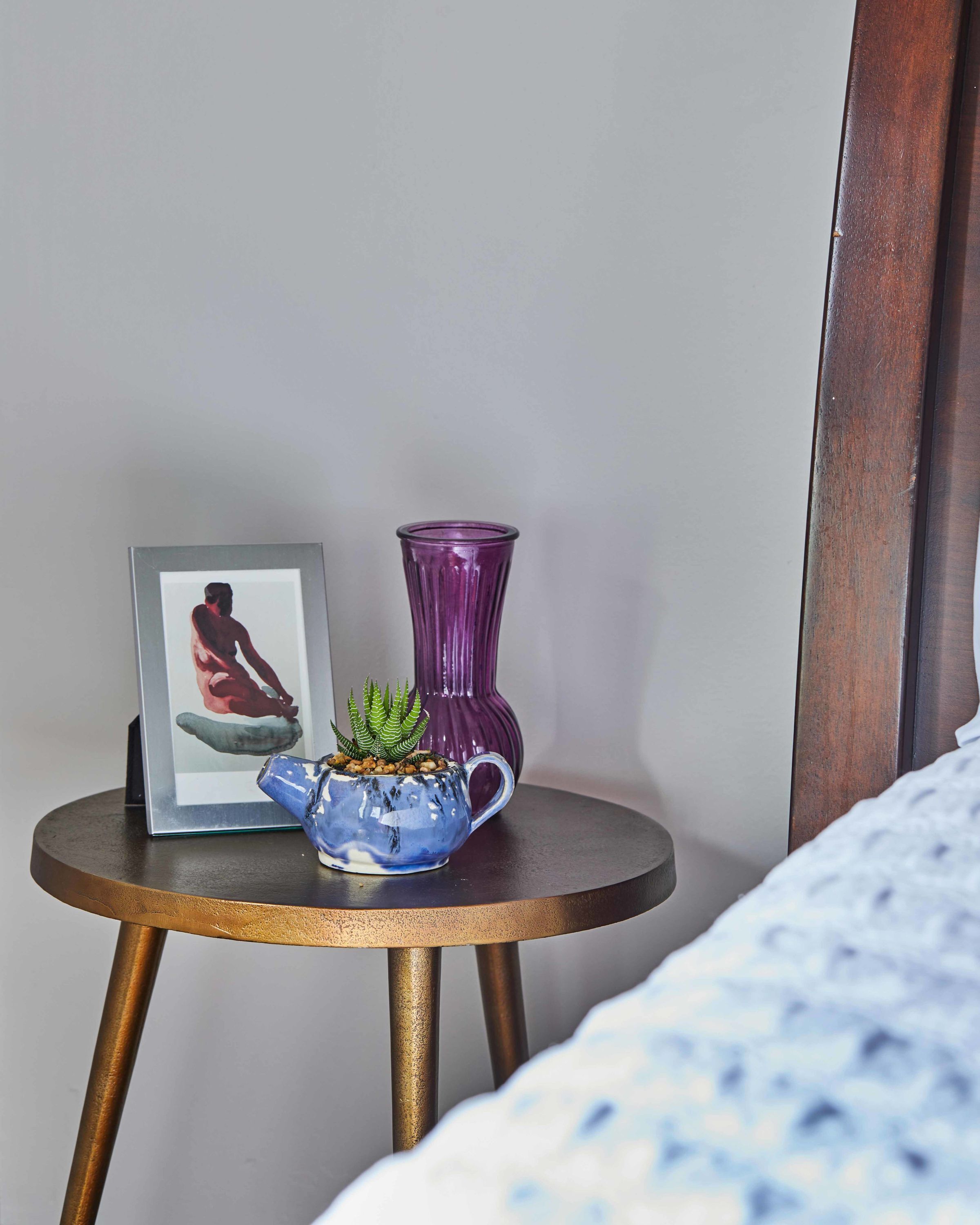 A small round table with a framed picture and two vases, one blue and one purple, against a plain wall.