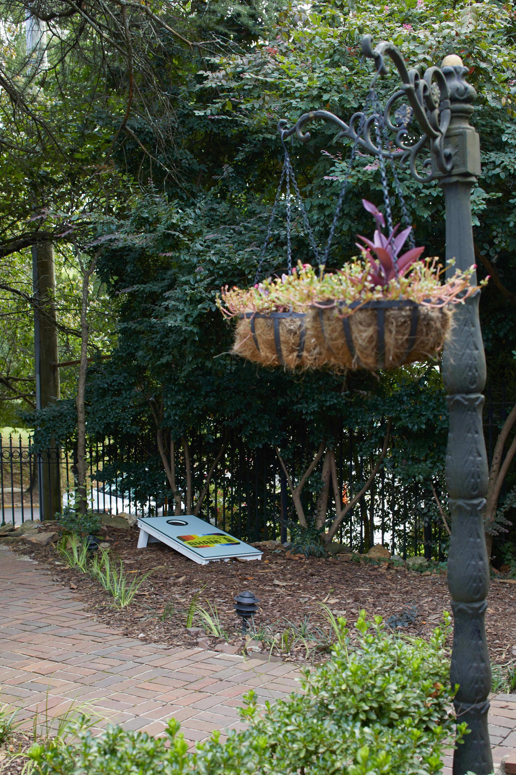 A hanging planter with plants, a paved walkway, and a metal fence in a garden setting.