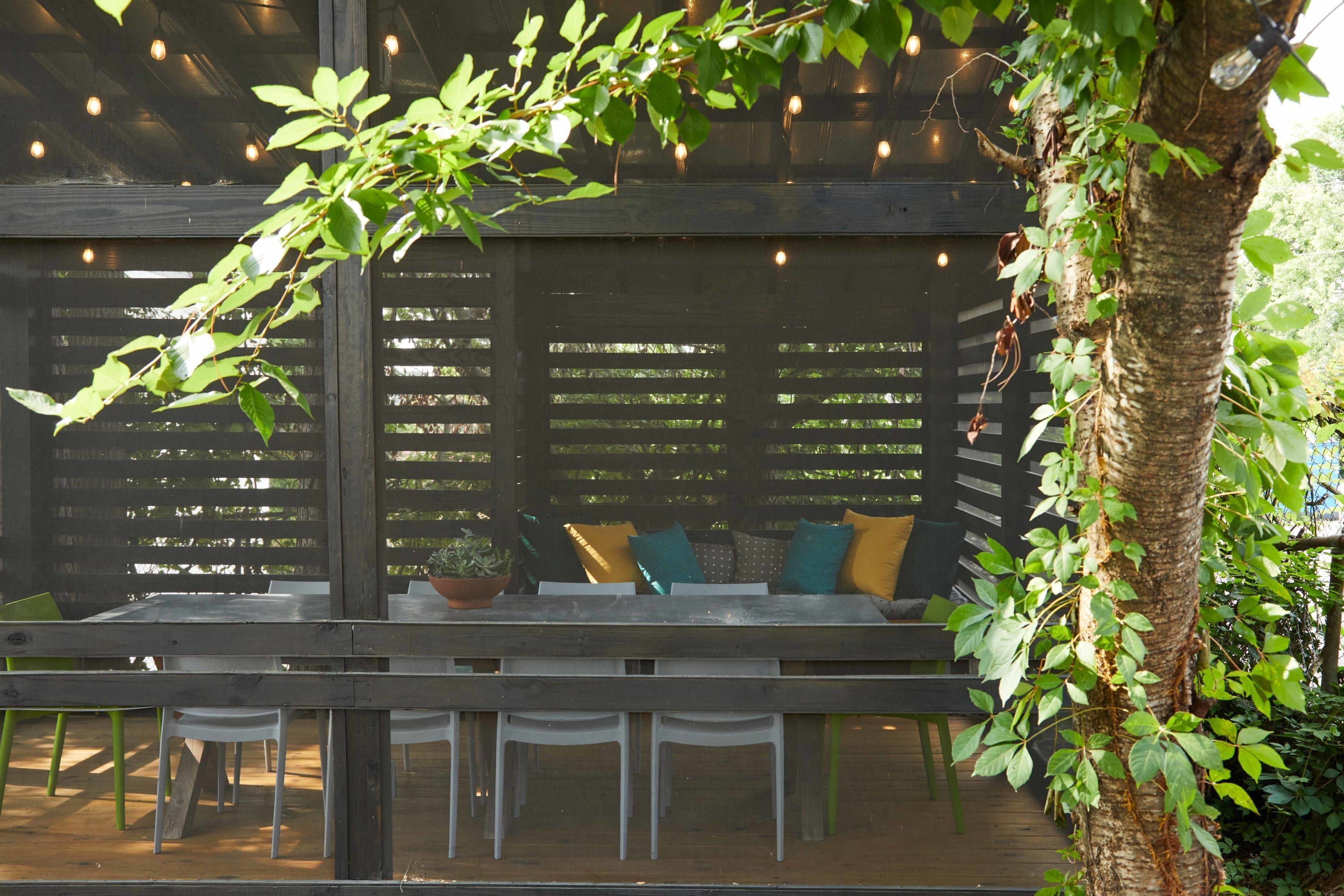 Un área de estar al aire libre con una mesa y sillas de madera, un banco acolchado y una planta en maceta.