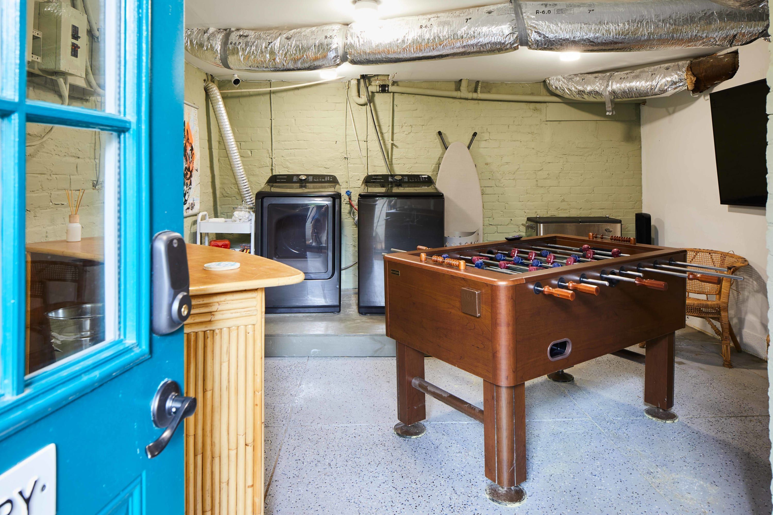 A room with a foosball table, a blue door, and two washing machines.