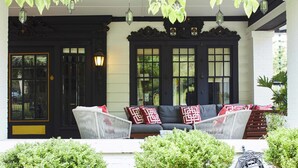 A porch with a black door, a white wall, and a black and white sofa with red and white cushions.