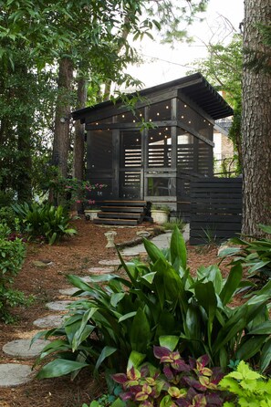 Une cabane en bois dotée d’un porche, entourée d’une végétation luxuriante et d’arbres.
