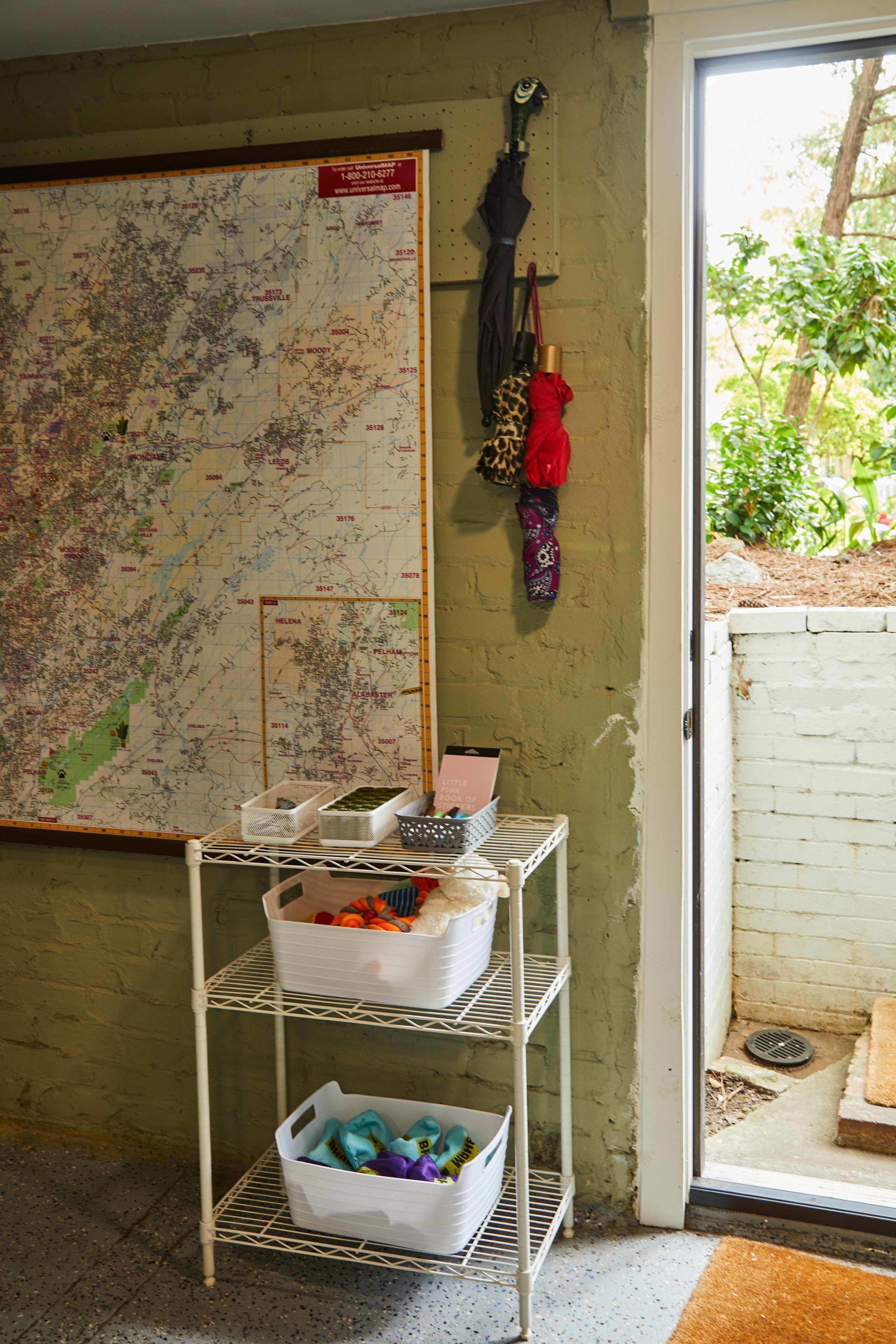 A room with a map on the wall, a white shelf with storage bins, and a door leading outside.