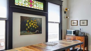 Un comedor con una mesa de madera larga, sillas, un mueble pequeño con electrodomésticos y obras de arte en las paredes.