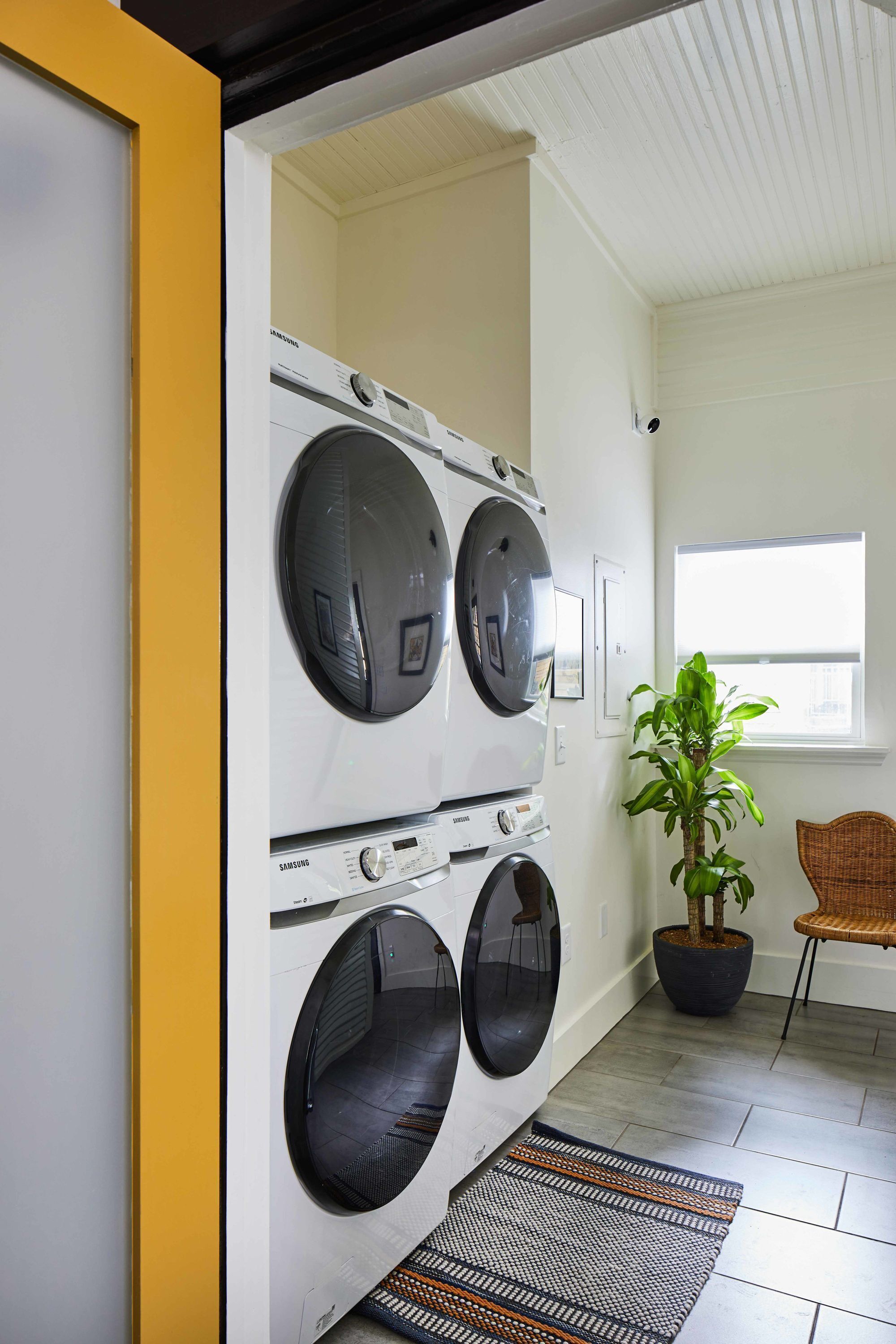 A laundry room with a white washing machine and dryer, a potted plant, and a wicker chair.