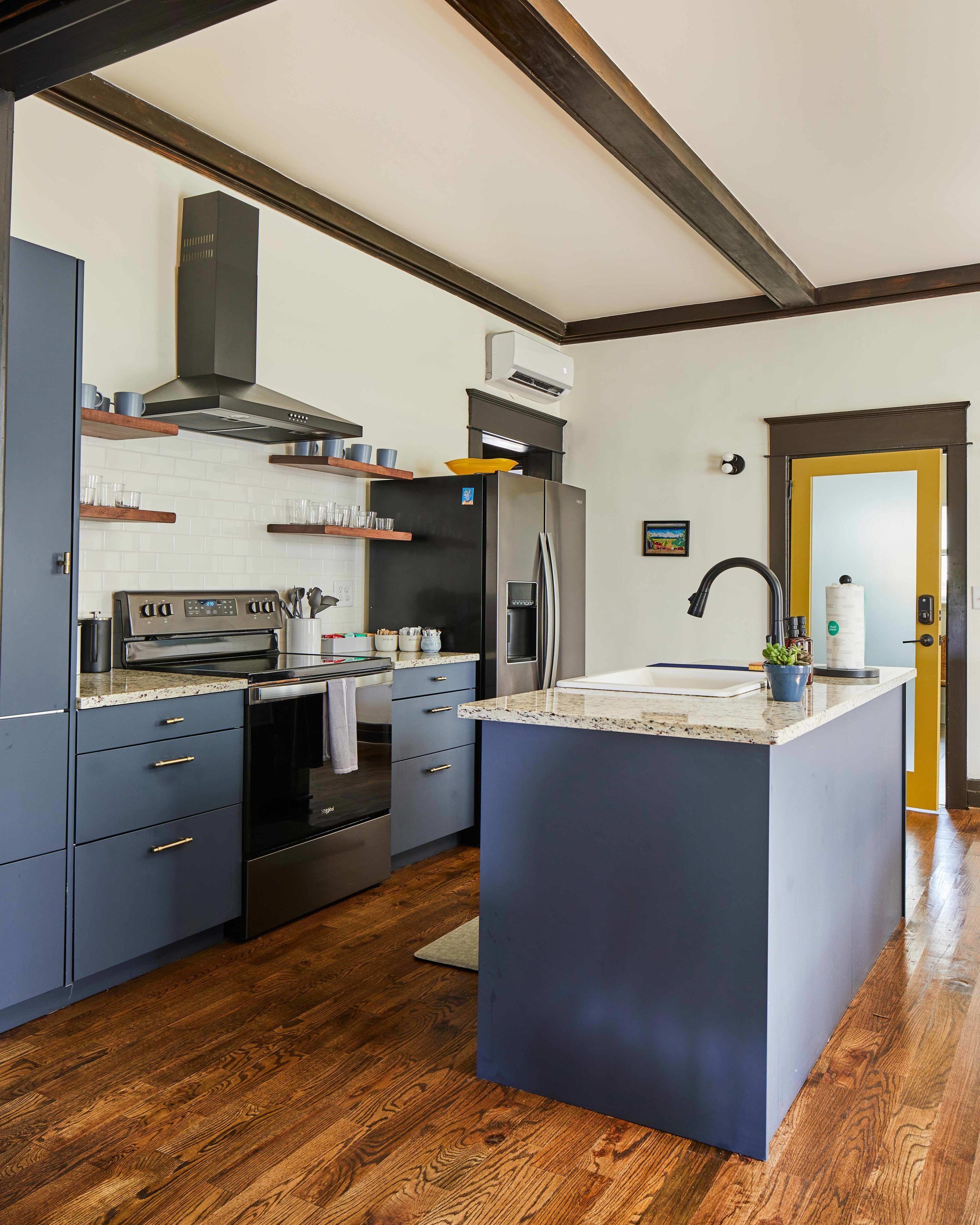 A modern kitchen with a central island, built-in oven, stainless steel appliances, and wooden flooring.
