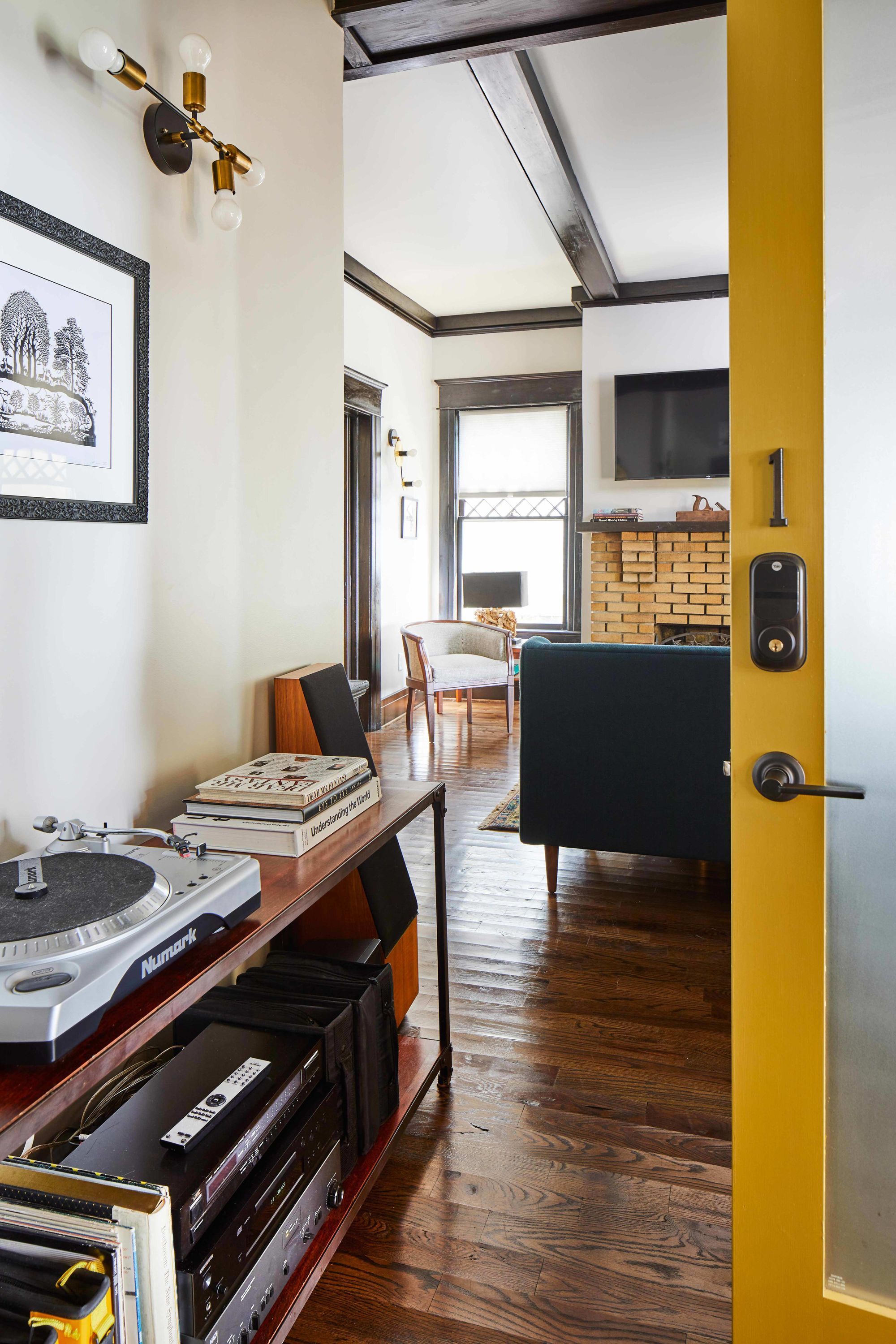 Una sala de estar moderna con piso de madera, un sofá negro, una mesa de centro y una estantería con libros y un tocadiscos.