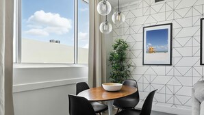 A dining area with a round wooden table, black chairs, a white bowl, and a framed picture on the wall.