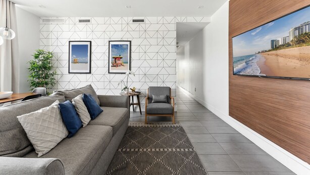 A modern living room with a grey sofa, a small round table, and a large TV screen displaying a beach scene.