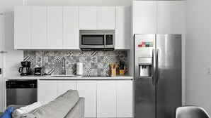 A modern kitchen with white cabinets, a stainless steel refrigerator, a microwave, and a coffee maker.