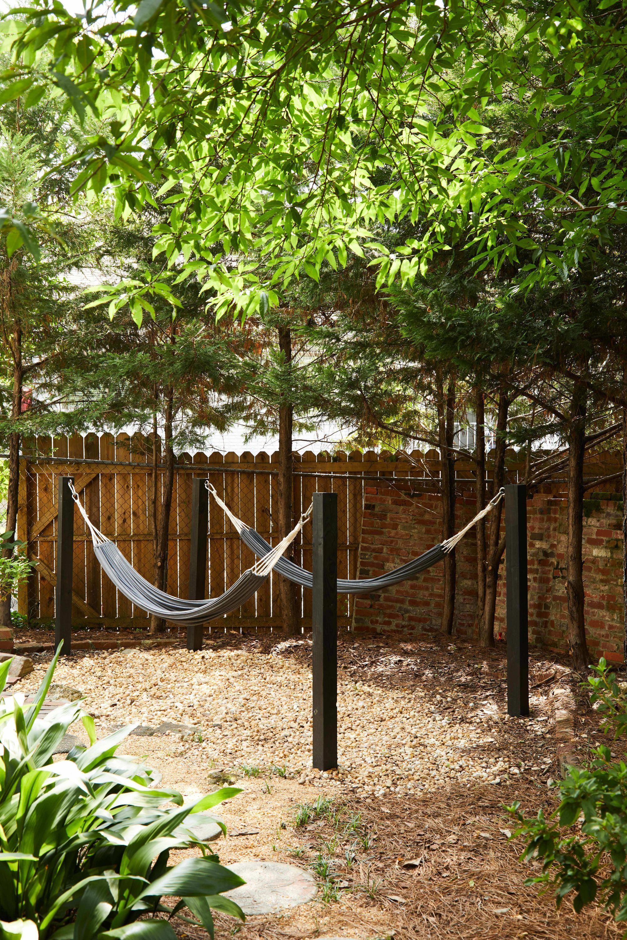 A hammock between two posts in a garden area with a brick wall and trees in the background.