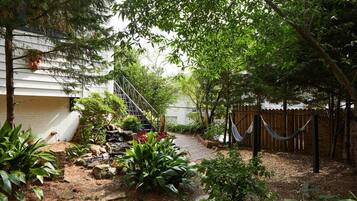 Un jardín con una escalera de madera que lleva a una casa, rodeado de diversas plantas y una hamaca.