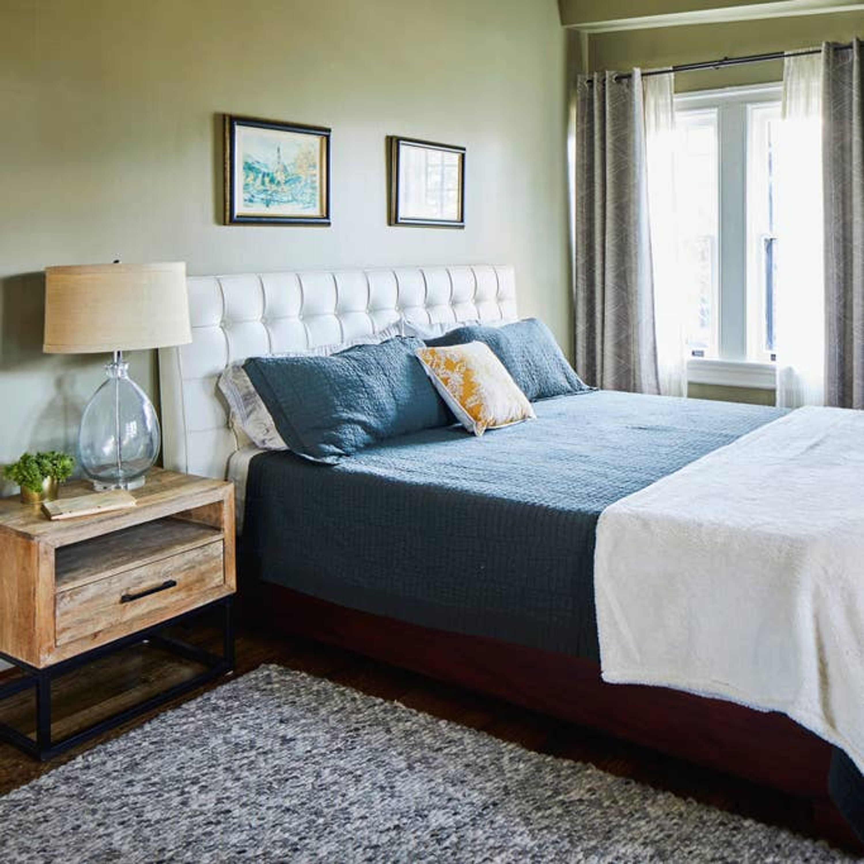 A bedroom with a large bed, a nightstand with a lamp, and two framed pictures on the wall.